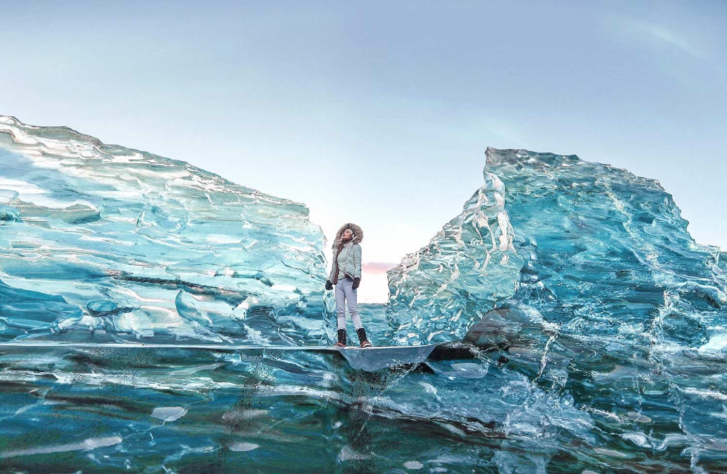 Traveler standing beside a wall of turquoise glacier ice on Iceland's diamond beach